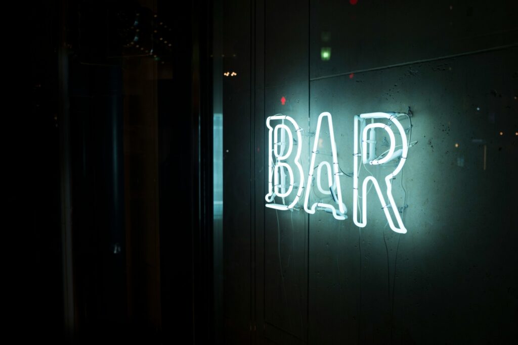 Illuminated neon "BAR" sign glowing against a dark background.