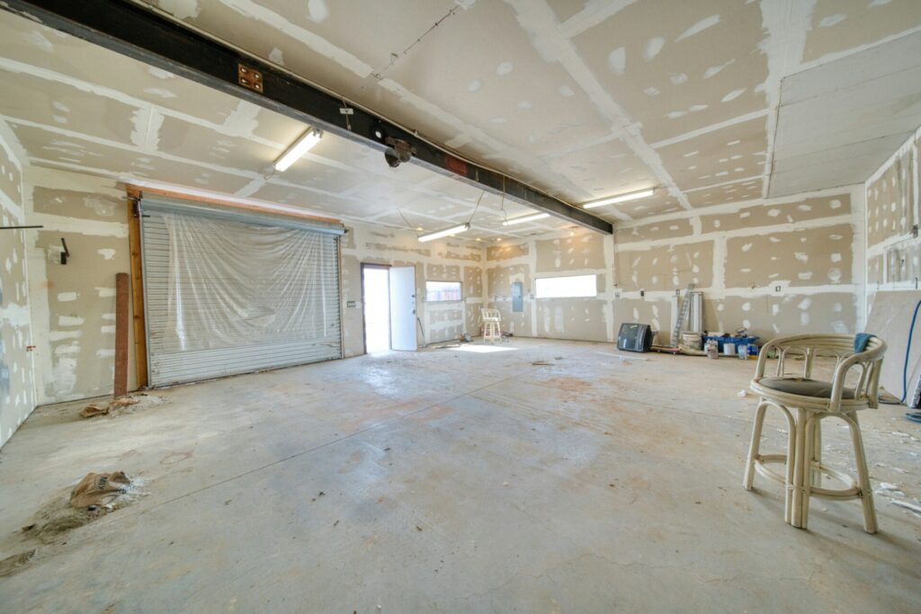 An empty, unfinished garage with scattered items and exposed drywall.