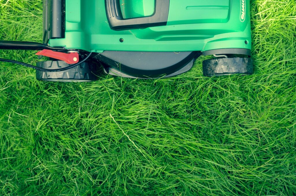 A green lawn mower on lush grass, viewed from above.
