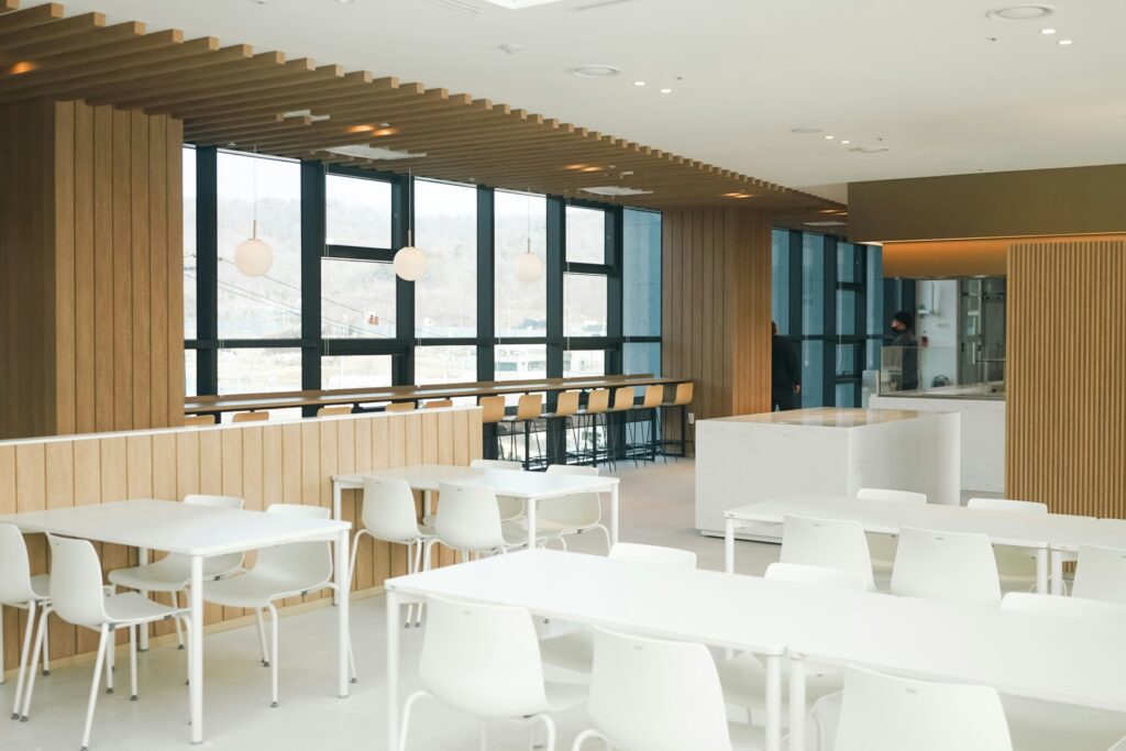 Modern cafeteria with wooden accents, white furniture, and large windows.
