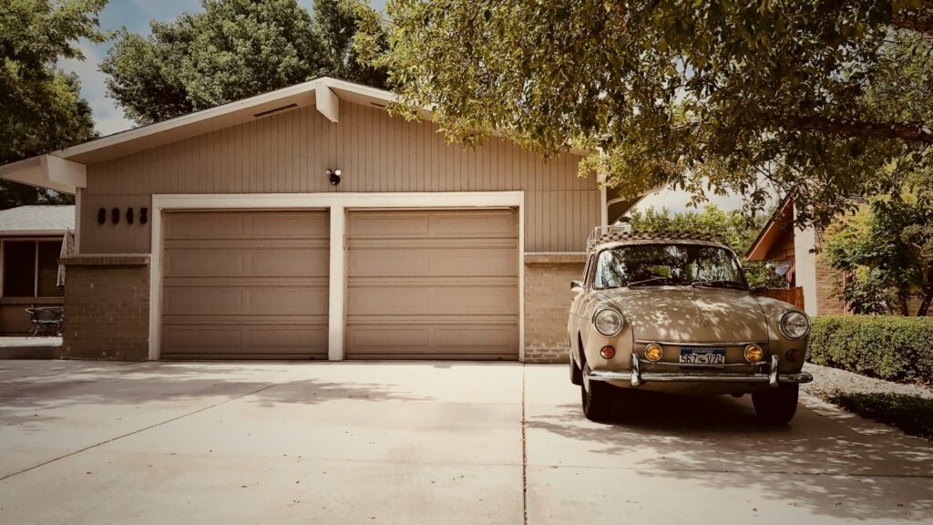 Vintage beige car parked in front of a suburban garage and driveway.