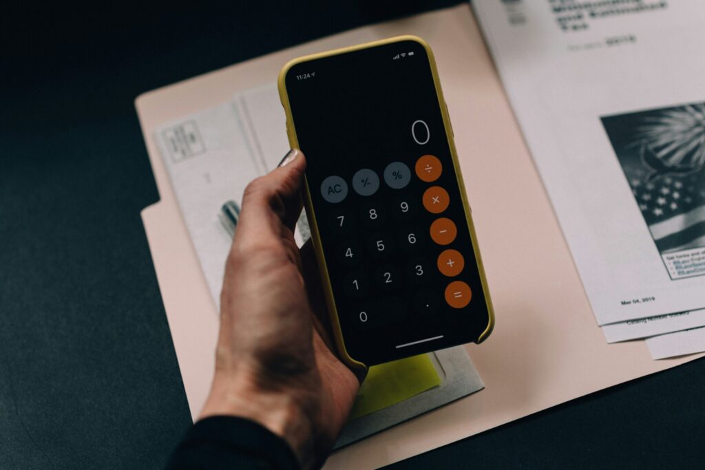 A person holds a smartphone displaying a calculator app over documents.