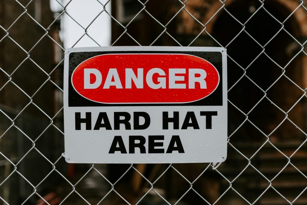 A "Danger: Hard Hat Area" sign on a chain-link fence at a construction site.