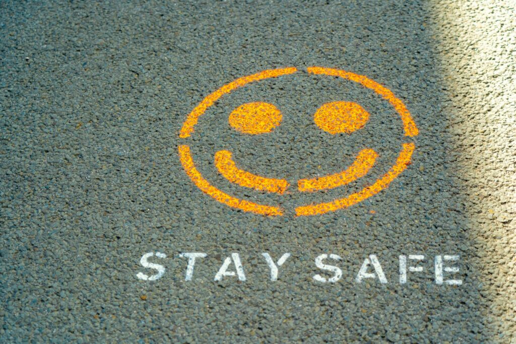 Smiley face and "STAY SAFE" painted on a rough asphalt surface.