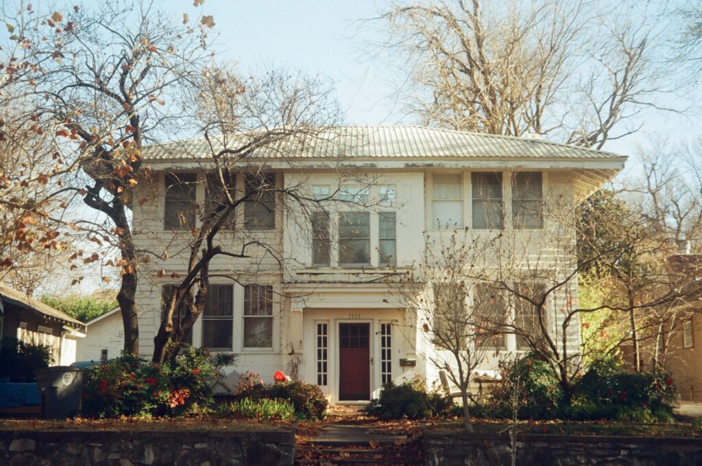 A vintage white house with a red door surrounded by bare trees.