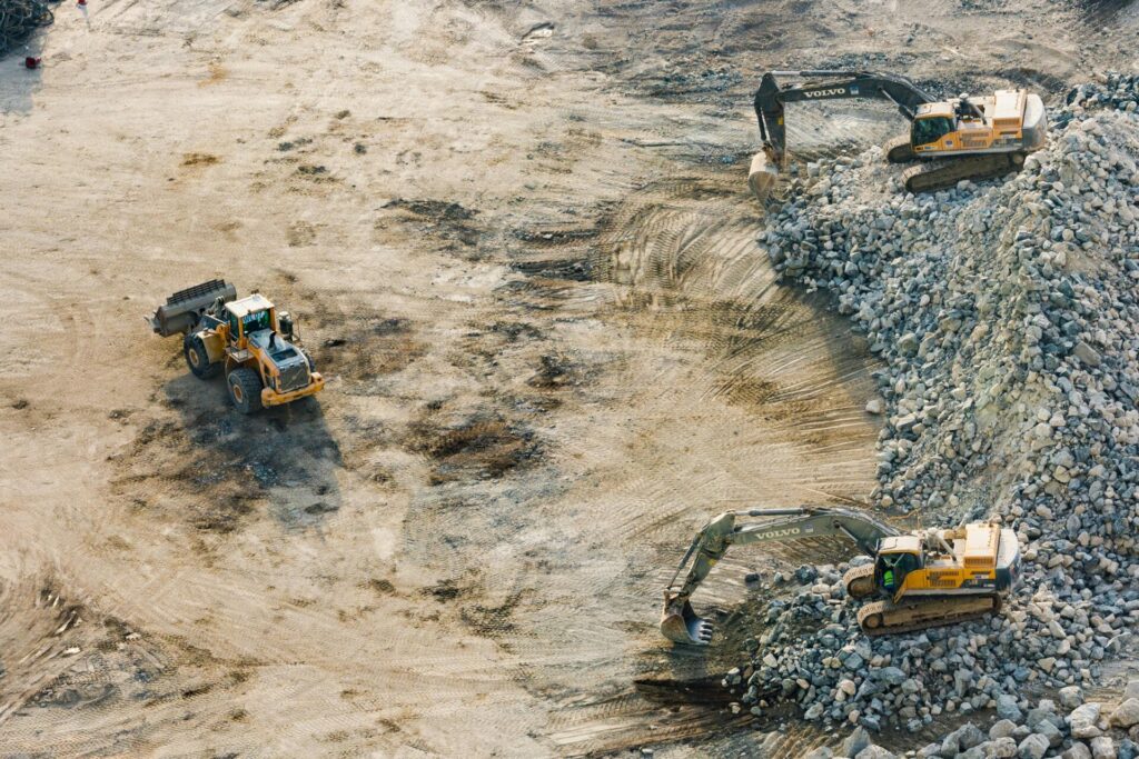 Two excavators move rocks on a construction site with dirt and debris.