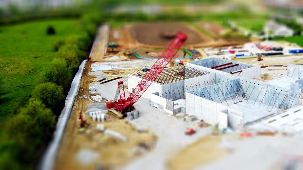 A red crane operates at a large construction site with unfinished concrete structures.