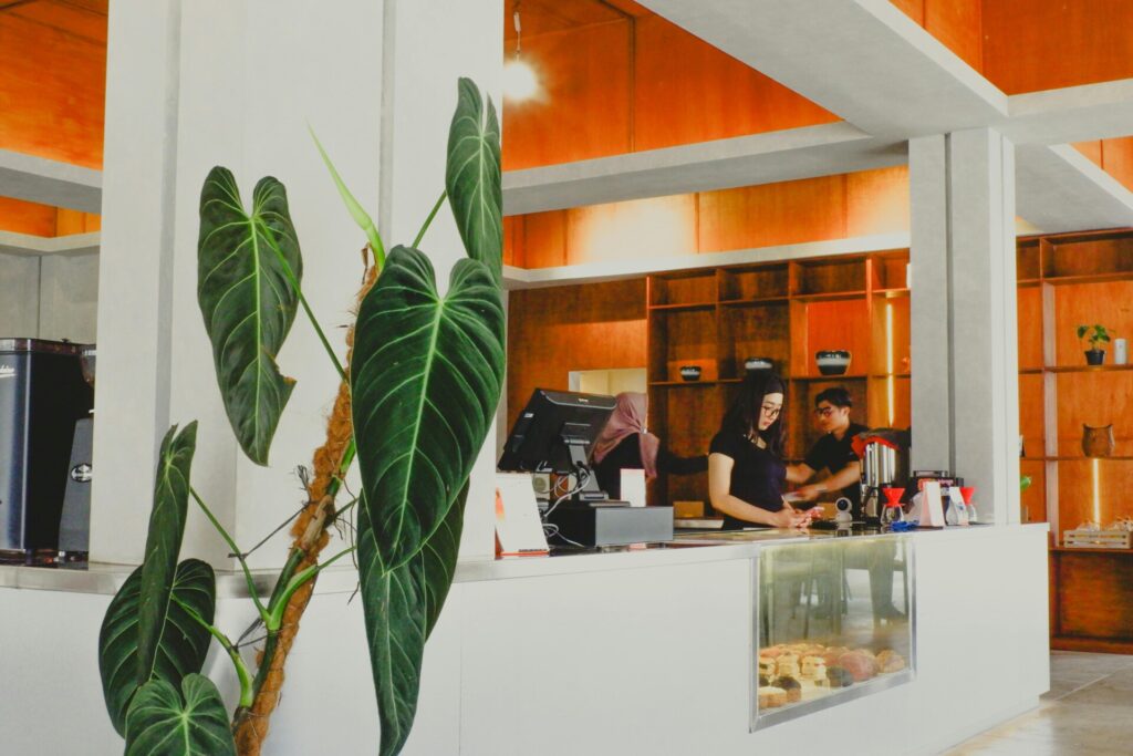 A modern coffee shop interior with staff behind the counter and large leaves.