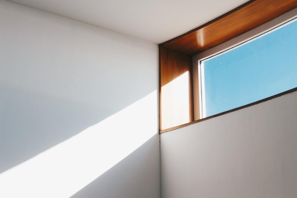 Sunlight casts a shadow through a window onto a white wall.