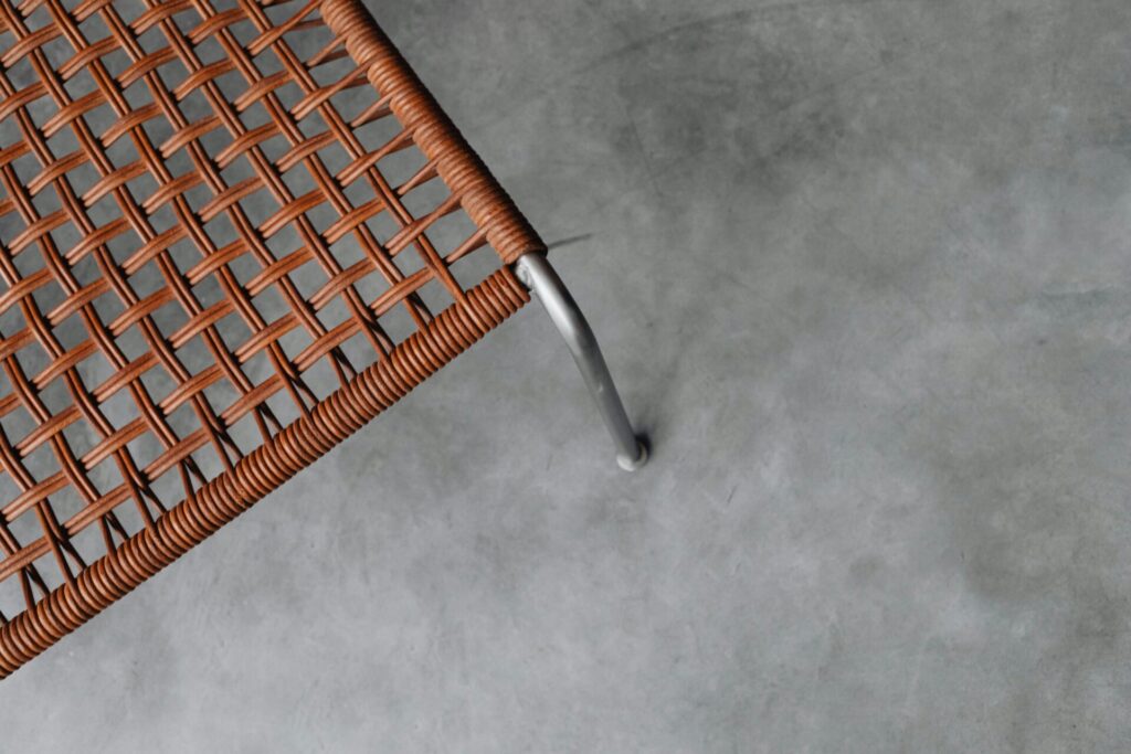Close-up of a woven brown rattan chair on a gray concrete floor.