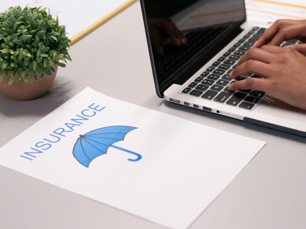 Person typing on a laptop beside a paper with an insurance icon.