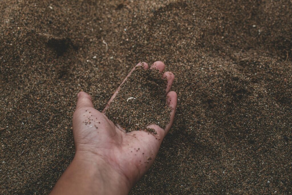 A hand holding dark beach sand against a background of more sand.