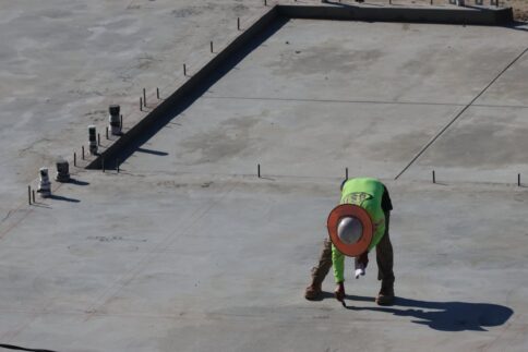 A construction worker in a green shirt marks a concrete surface.