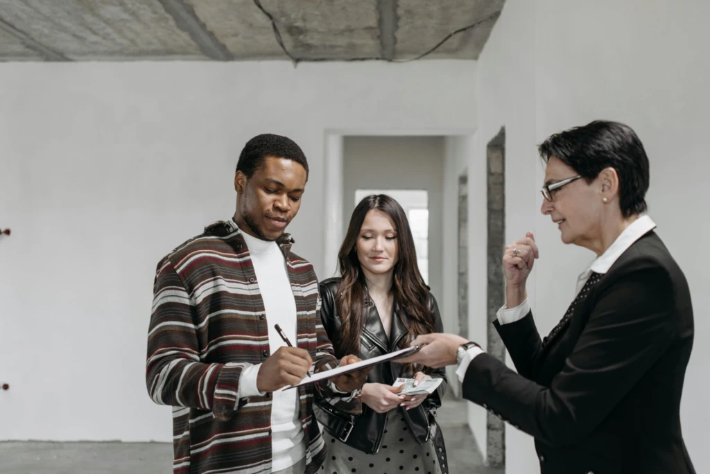 Three people in an unfinished room signing documents.