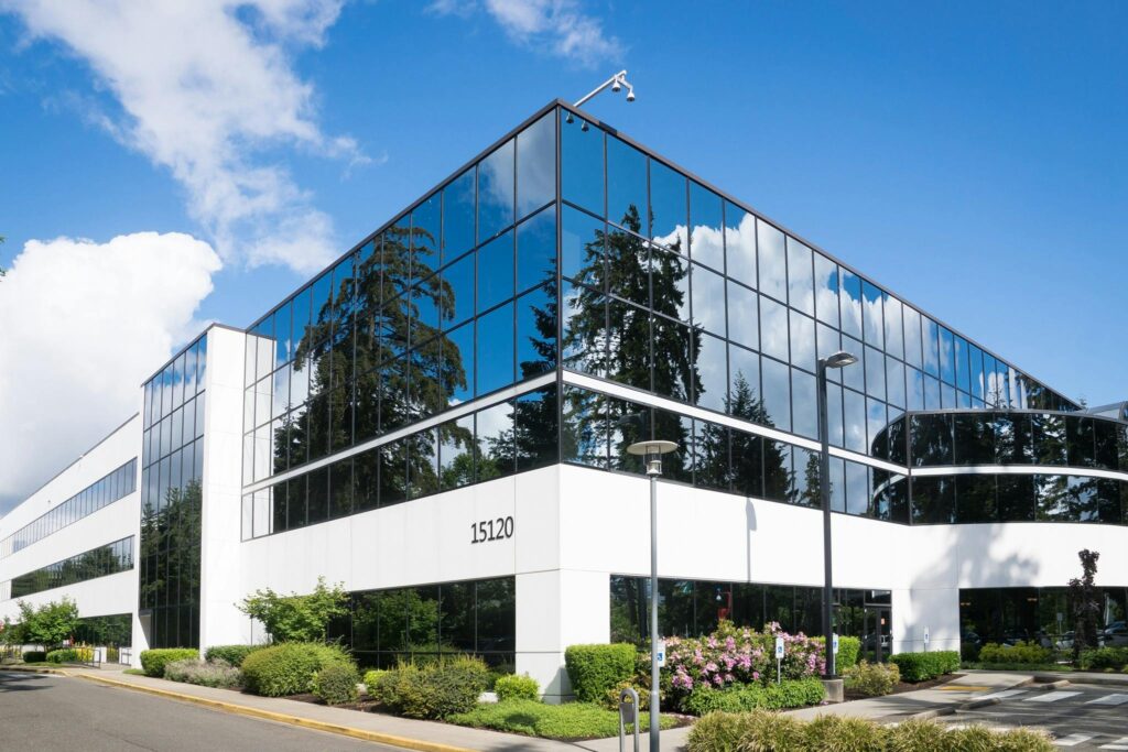 Modern glass office building with trees and sky reflecting on its windows.
