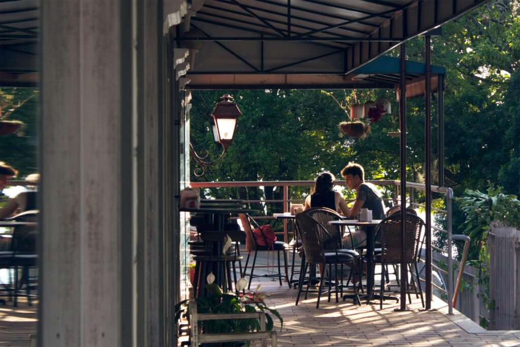A couple sits at an outdoor café, surrounded by greenery.