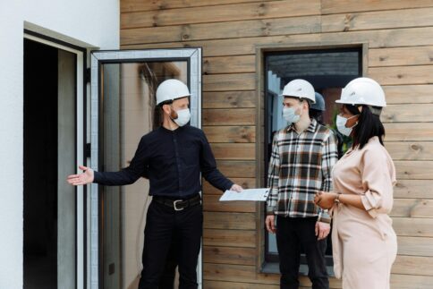 Three people in hard hats discuss at a construction site.