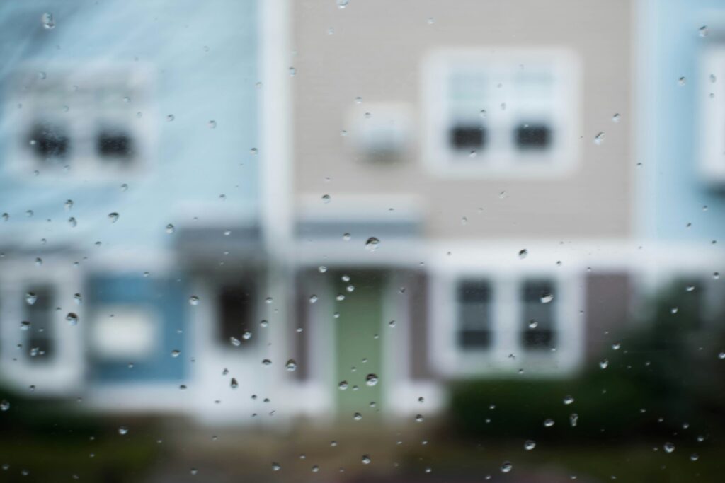Raindrops on a window with blurred houses in the background.