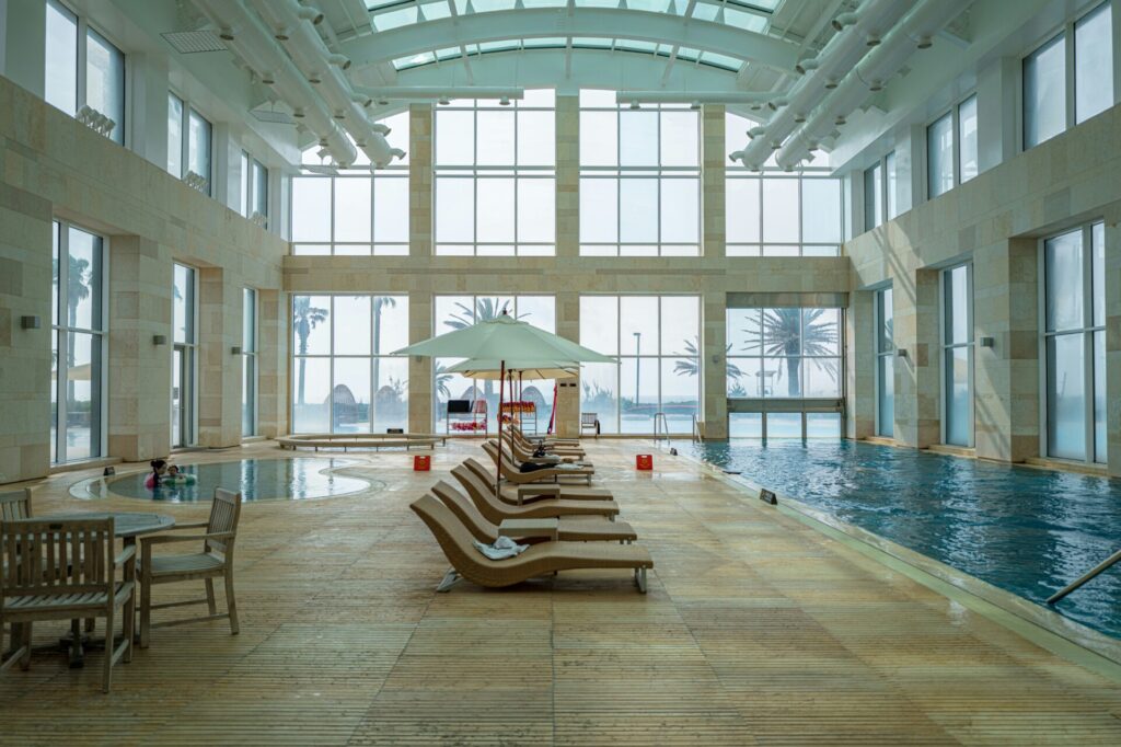 Indoor pool area with lounge chairs, large windows, and palm tree views.