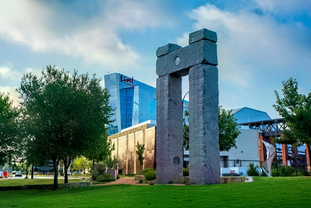Stone monument in a green park with modern buildings in the background.