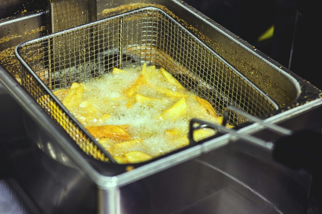 Golden french fries frying in hot oil within a metal deep fryer basket.
