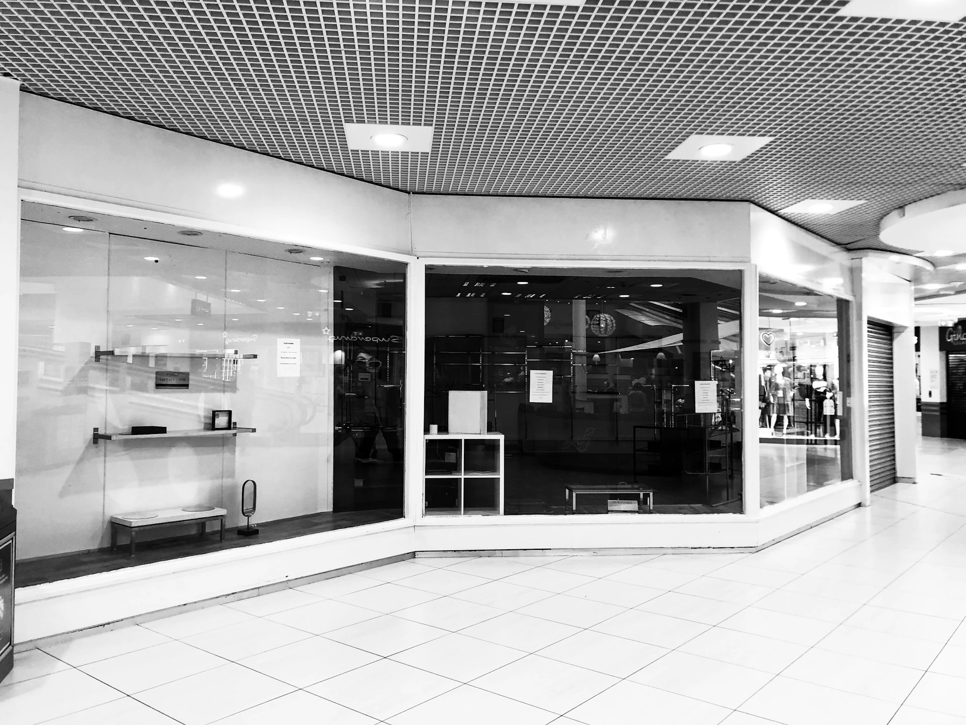 Empty storefront in a shopping mall with reflective glass displays.