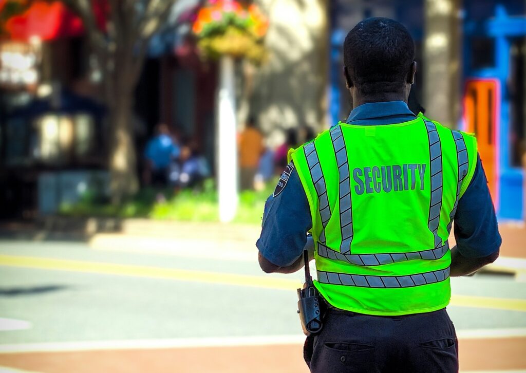 Security guard in a bright vest stands on a city street.