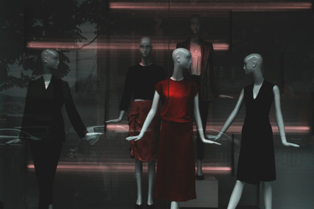 Mannequins dressed in stylish outfits displayed in a dimly lit window.