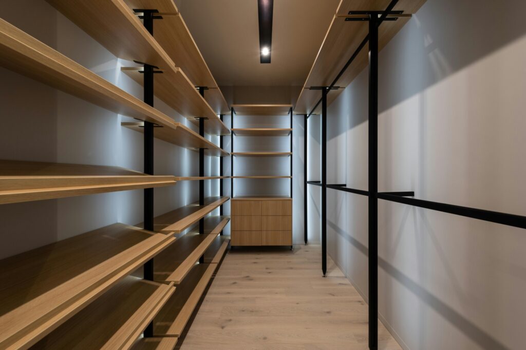 Empty walk-in closet with wooden shelves and modern black supports.