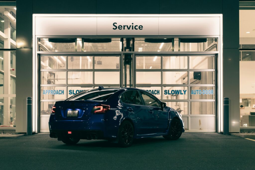 A blue car is parked outside a service center with illuminated signage.