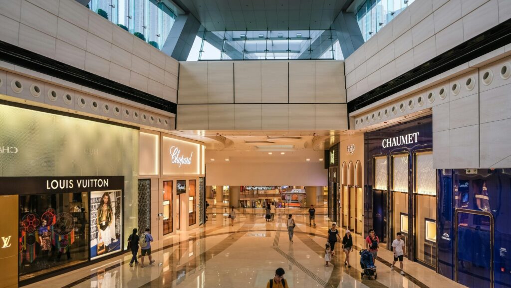Shoppers walk through a luxurious indoor mall featuring high-end brand stores.