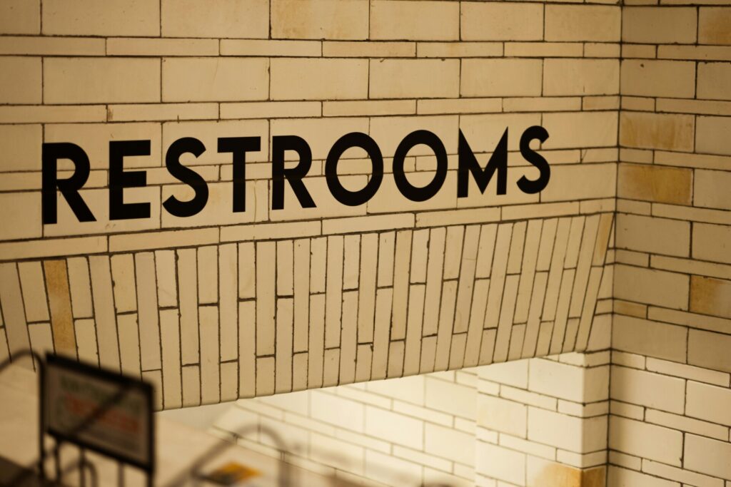 Restroom sign on a tiled wall with a staircase leading down.