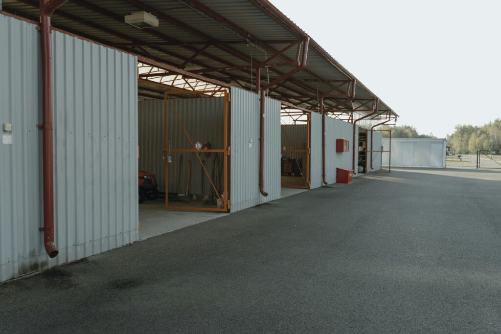 A row of open metal storage units near an empty paved area.