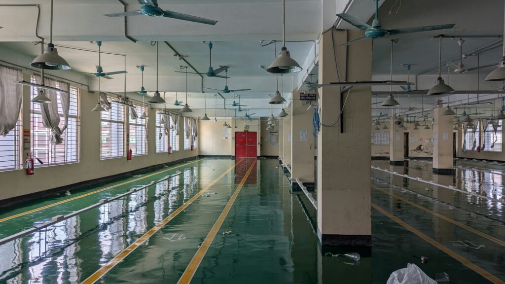 An empty factory floor with ceiling fans and wet, reflective green flooring.