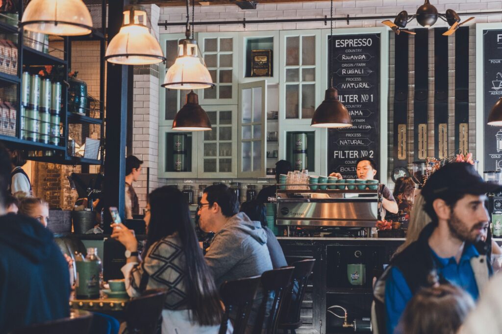A busy cafe with people enjoying drinks and a barista preparing coffee.