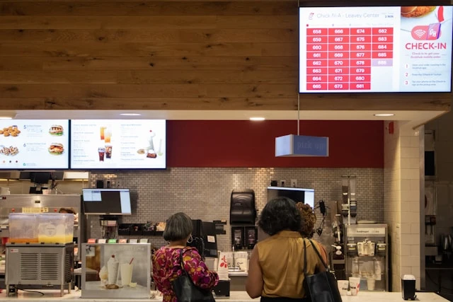 Two people wait at a fast-food counter in a modern restaurant.