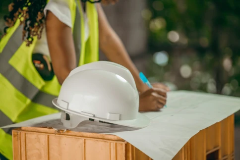 A construction worker writes on a blueprint with a hard hat nearby.
