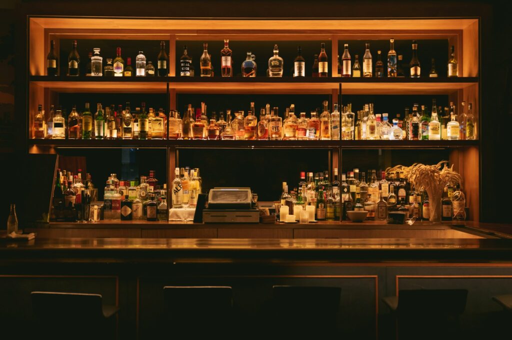 A dimly lit bar shelf displaying a variety of liquor bottles.