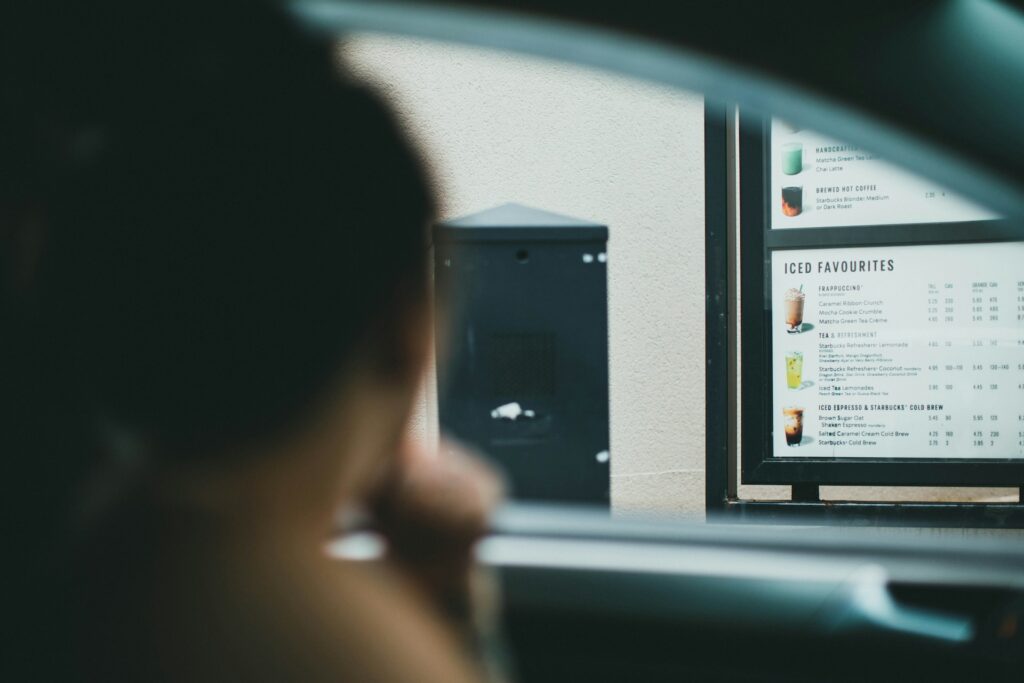Person in a car at a drive-thru lane viewing a menu board.