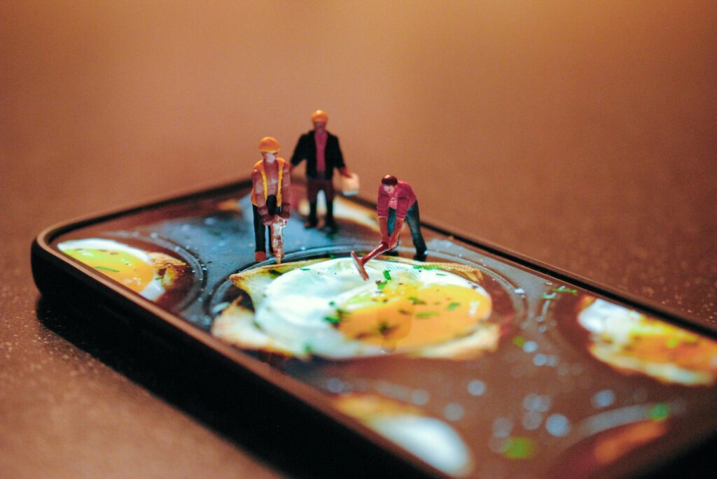 Miniature workers on a smartphone screen depicting fried eggs being prepared.