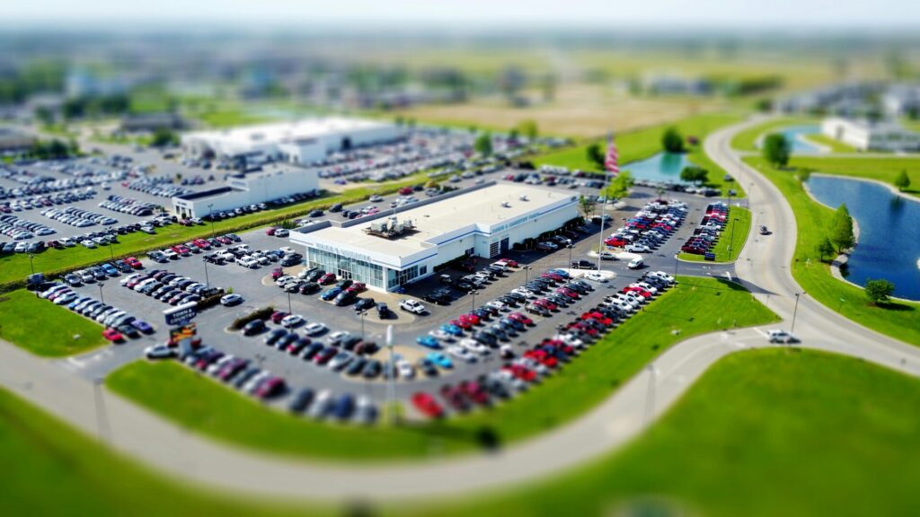 Aerial view of a busy car dealership with parked vehicles and surrounding roads.