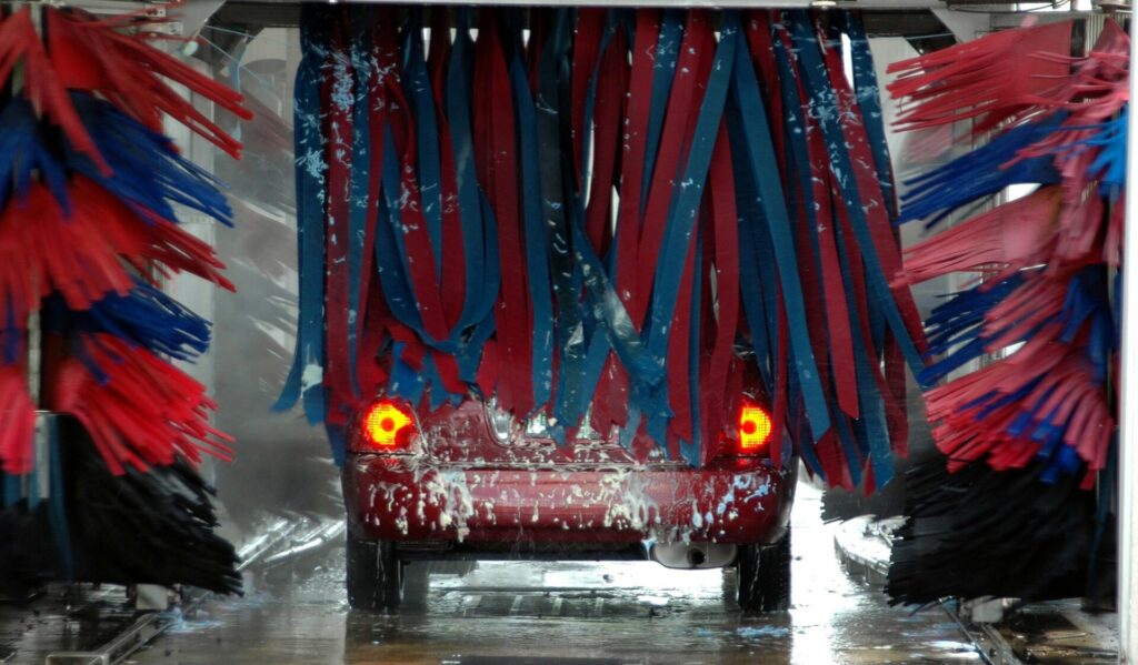 A red car in an automated car wash with brushes and soap.