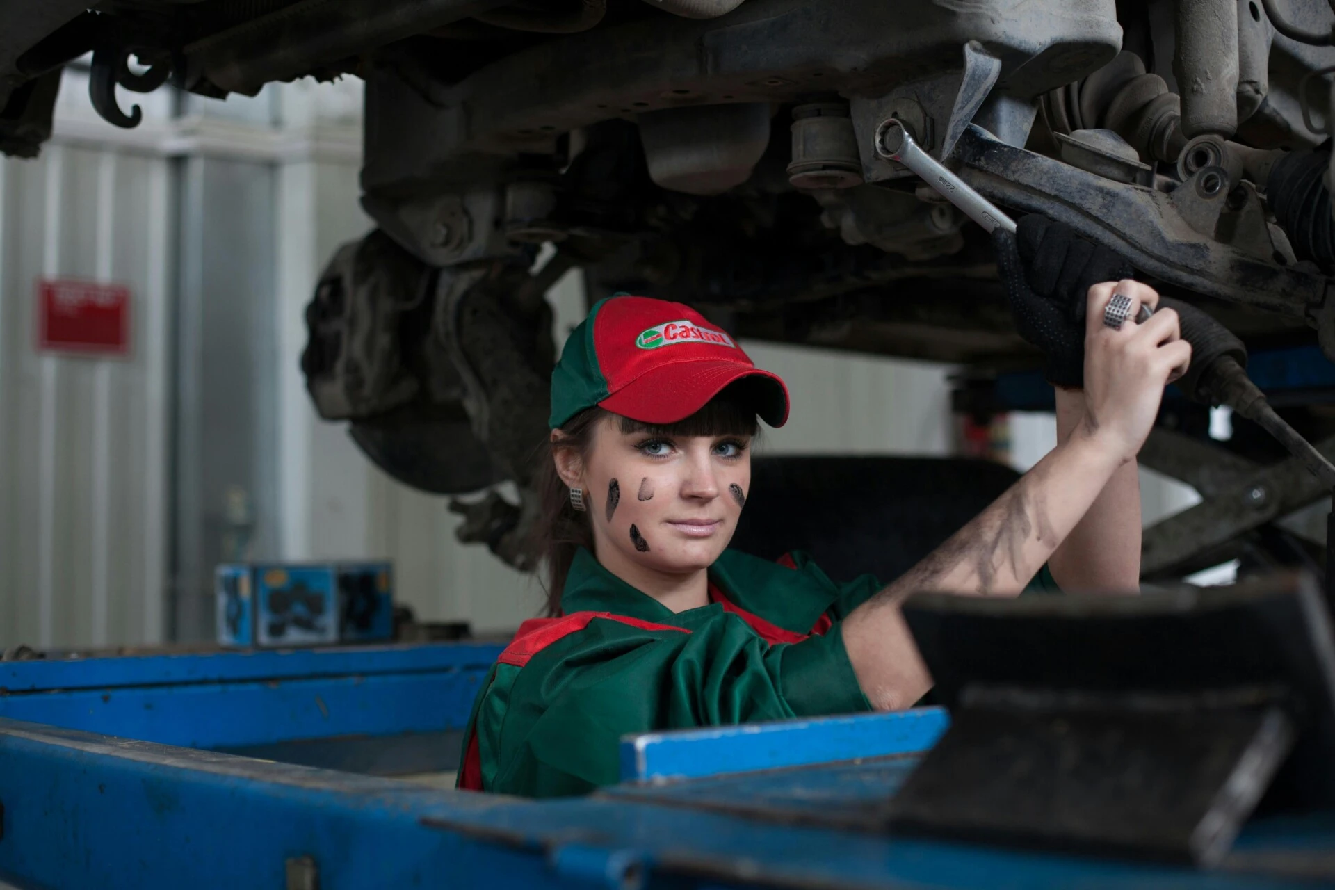 A female mechanic in uniform works on a car in a garage.