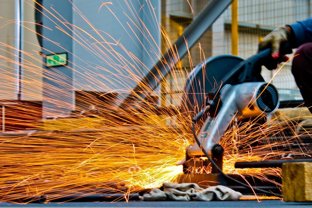 A worker uses a cutting tool, creating bright orange sparks in a workshop.