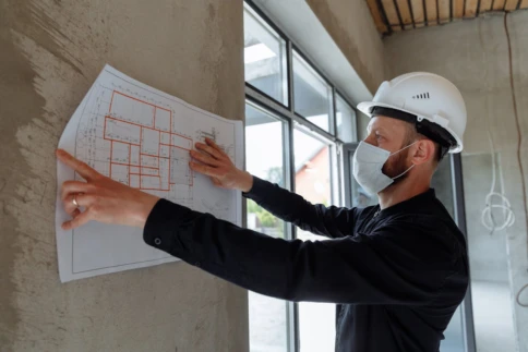 A construction worker examines architectural plans on a wall inside a building.