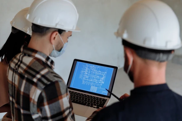 Three construction workers reviewing a blueprint on a laptop screen.