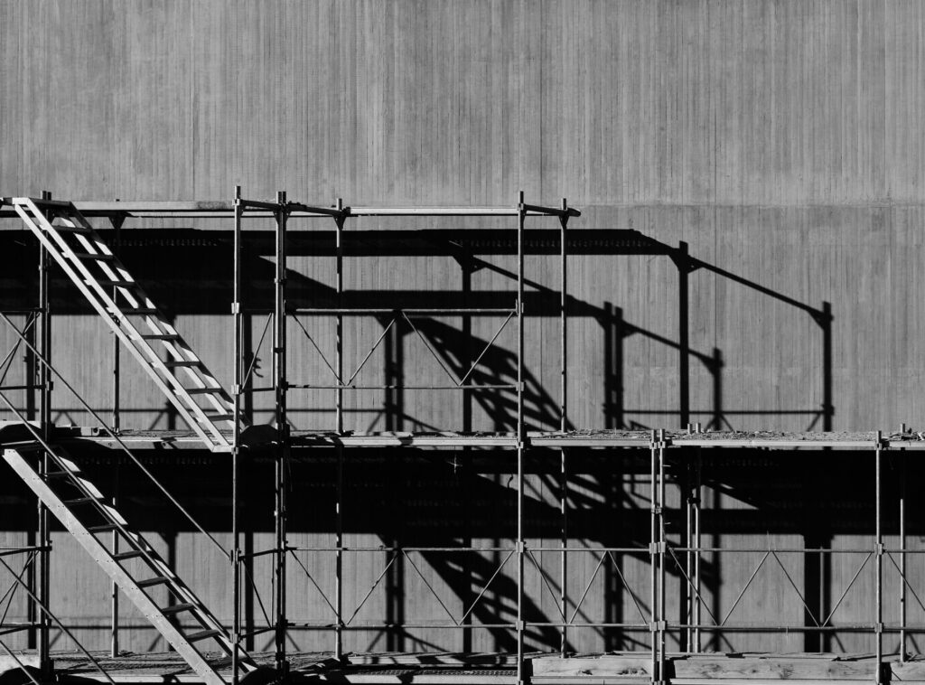 Scaffolding casts a shadow on a concrete wall under bright sunlight.