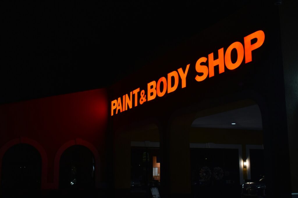 A brightly lit paint and body shop sign glows in the night.