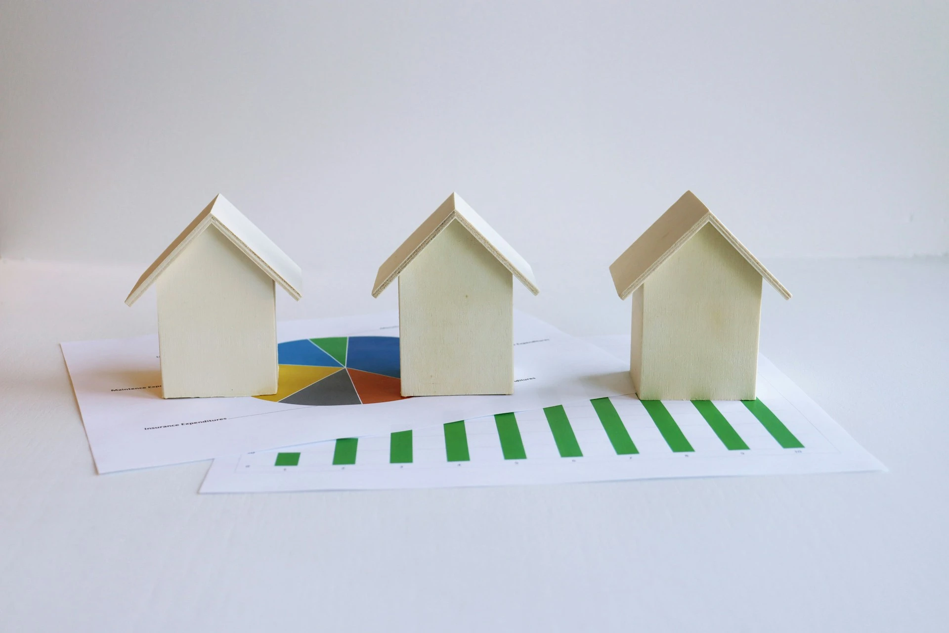 Three wooden house models on financial charts with graphs and pie charts.
