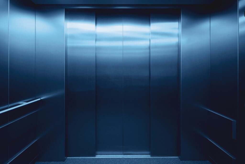 A dark, metallic elevator interior bathed in moody blue lighting.
